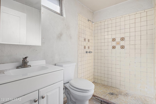 bathroom featuring toilet, a tile shower, and vanity