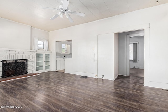 unfurnished living room featuring ceiling fan, a healthy amount of sunlight, a brick fireplace, and dark hardwood / wood-style floors