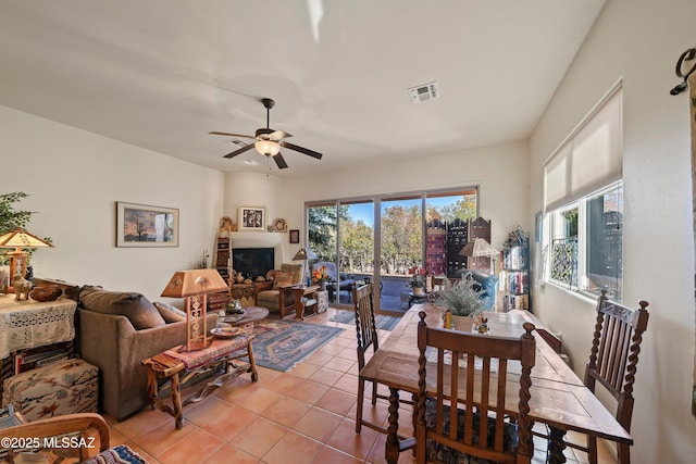 dining space featuring ceiling fan, a fireplace, and light tile patterned flooring