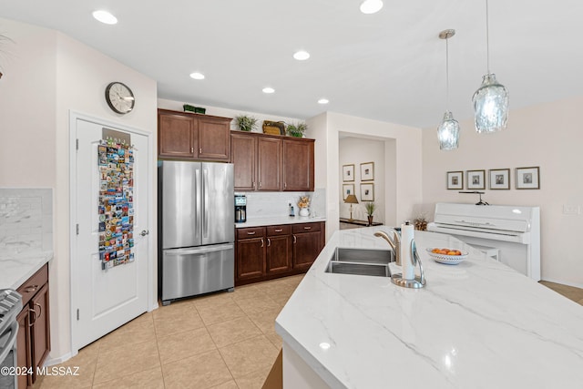 kitchen with pendant lighting, light tile patterned floors, stainless steel refrigerator, tasteful backsplash, and light stone countertops