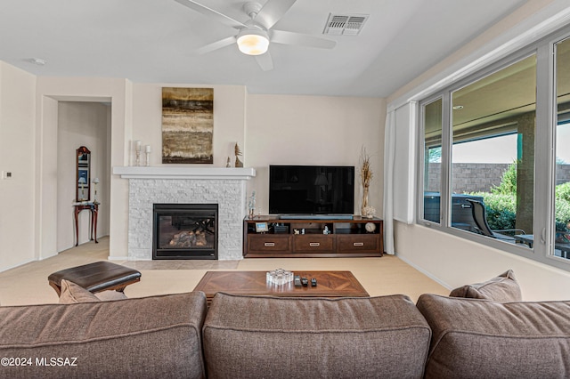 carpeted living room featuring a stone fireplace and ceiling fan