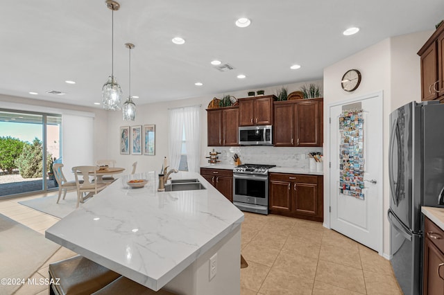 kitchen featuring a kitchen island with sink, sink, hanging light fixtures, and appliances with stainless steel finishes