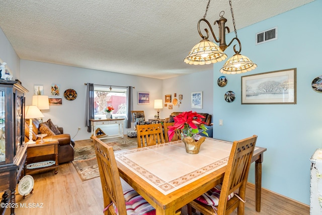 dining area with a textured ceiling and light hardwood / wood-style floors