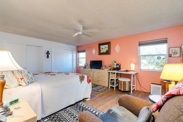 bedroom with ceiling fan, light hardwood / wood-style flooring, a textured ceiling, and two closets