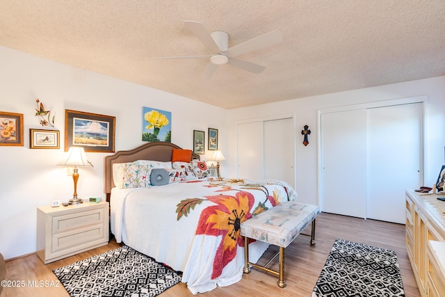 bedroom with two closets, a textured ceiling, ceiling fan, and light hardwood / wood-style floors