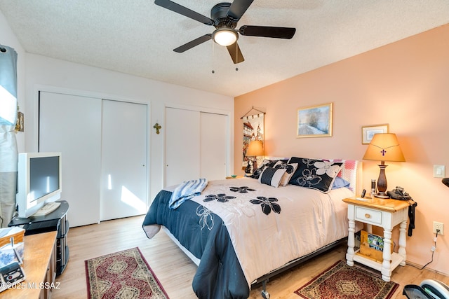 bedroom with two closets, light hardwood / wood-style flooring, a textured ceiling, and ceiling fan