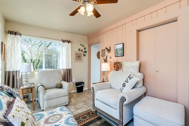 living room with light tile patterned flooring, ceiling fan, and wood walls