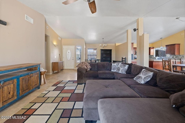 living room with vaulted ceiling, a wealth of natural light, and ceiling fan with notable chandelier