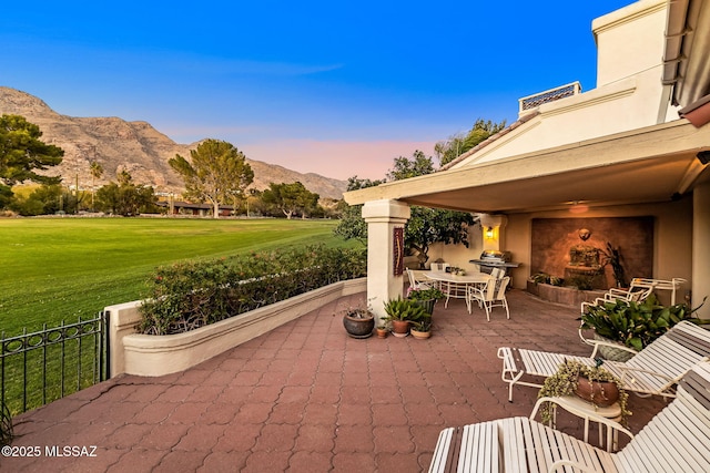 patio terrace at dusk with grilling area, a yard, and a mountain view