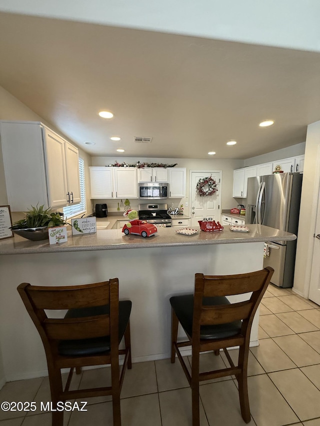 kitchen with kitchen peninsula, white cabinets, light tile patterned floors, and stainless steel appliances