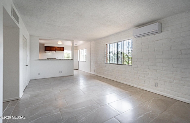 unfurnished living room featuring brick wall, a wall unit AC, and a textured ceiling