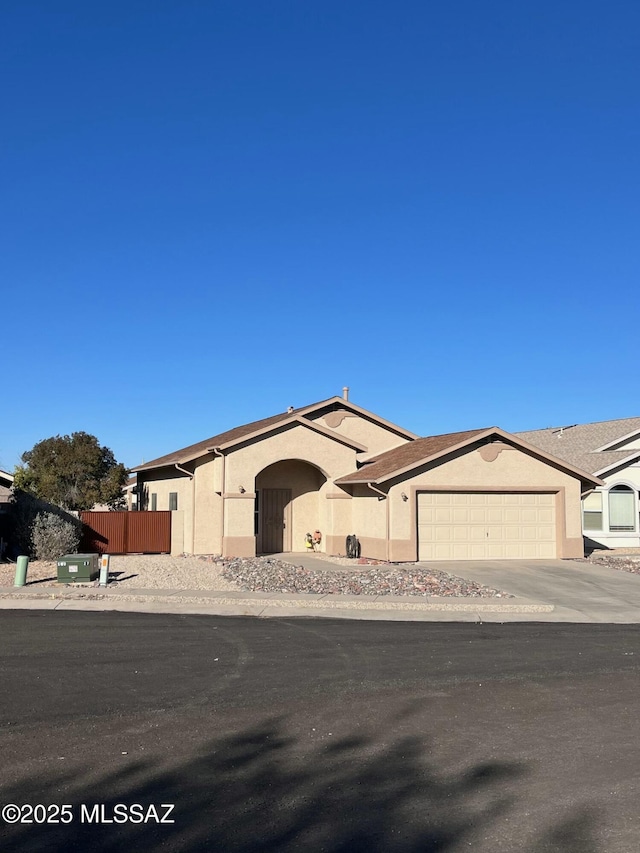 view of front of home featuring driveway, an attached garage, fence, and stucco siding