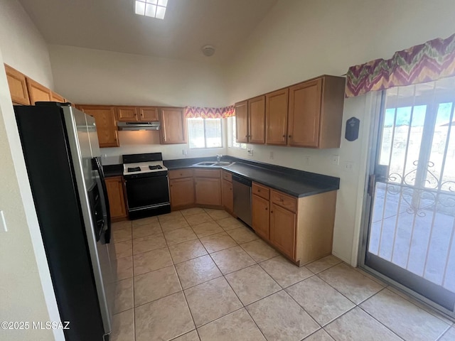 kitchen with dark countertops, appliances with stainless steel finishes, light tile patterned flooring, a sink, and high vaulted ceiling