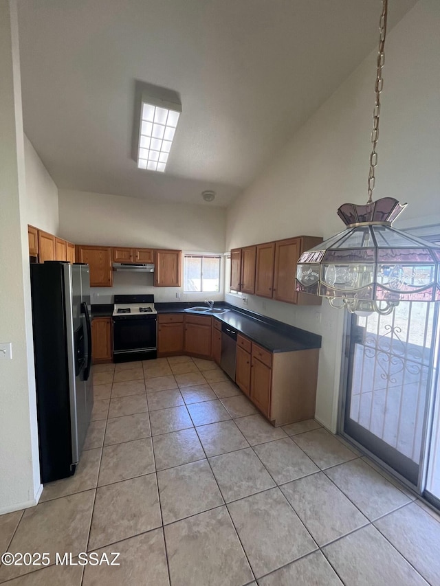 kitchen with under cabinet range hood, a sink, dark countertops, appliances with stainless steel finishes, and light tile patterned flooring