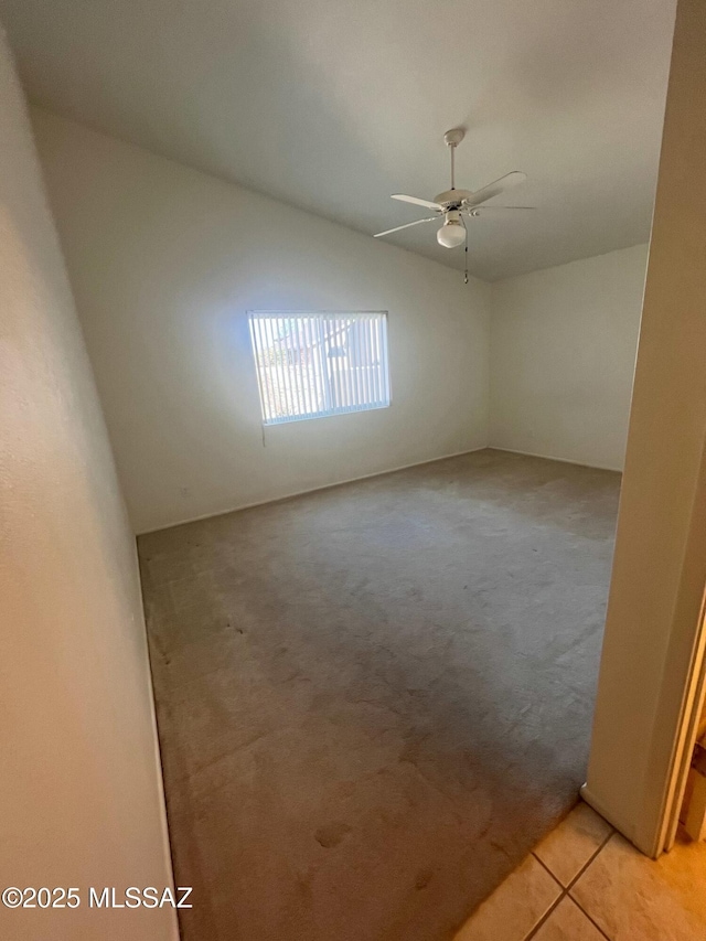 spare room featuring a ceiling fan, lofted ceiling, light colored carpet, and light tile patterned floors