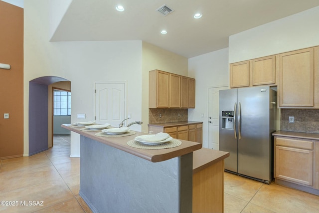 kitchen featuring stainless steel refrigerator with ice dispenser, a center island with sink, light brown cabinetry, and light tile patterned flooring