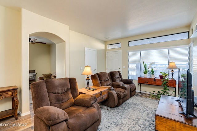 living room with arched walkways, baseboards, light wood-style flooring, and a ceiling fan