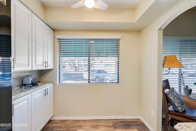 interior space featuring baseboards, arched walkways, a ceiling fan, and wood finished floors