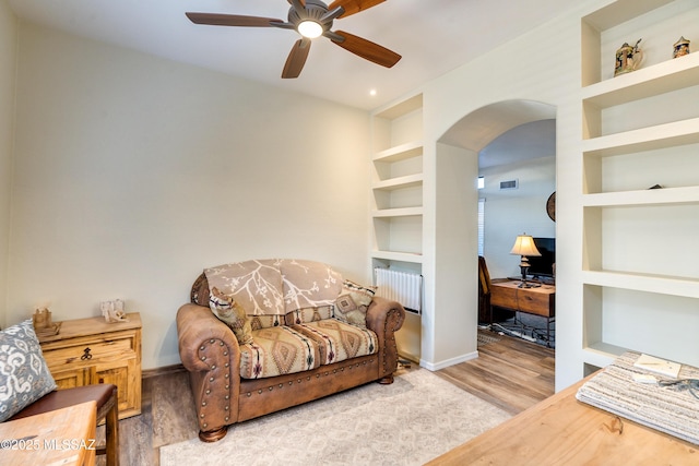 living room with arched walkways, ceiling fan, built in shelves, wood finished floors, and baseboards