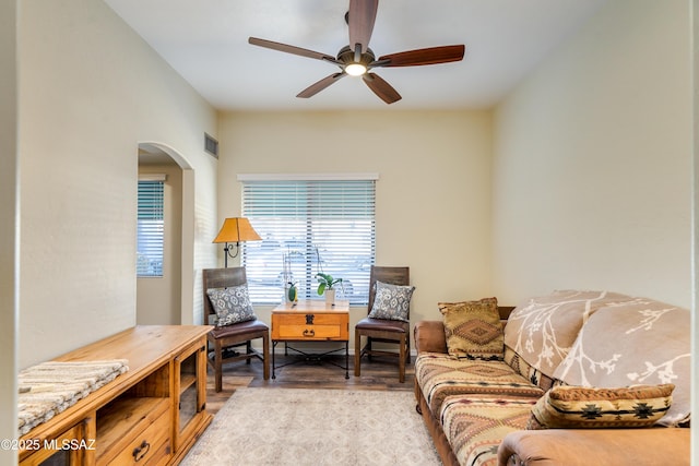 living area with ceiling fan, light wood finished floors, arched walkways, and visible vents