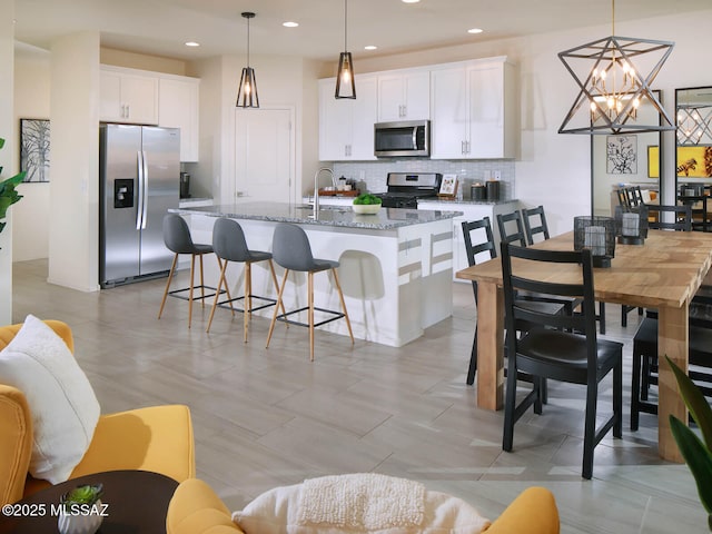 kitchen with appliances with stainless steel finishes, white cabinetry, backsplash, dark stone counters, and hanging light fixtures