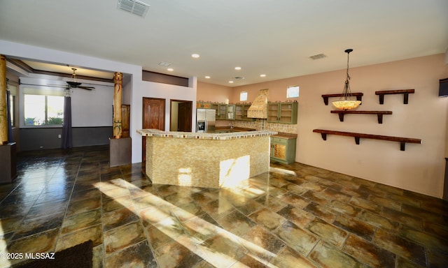 kitchen with ceiling fan, decorative light fixtures, stainless steel fridge, and a center island with sink