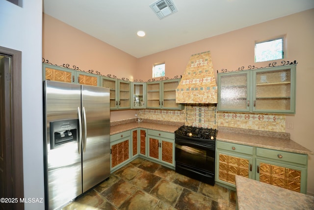 kitchen with stainless steel refrigerator with ice dispenser, decorative backsplash, black gas range, and custom range hood