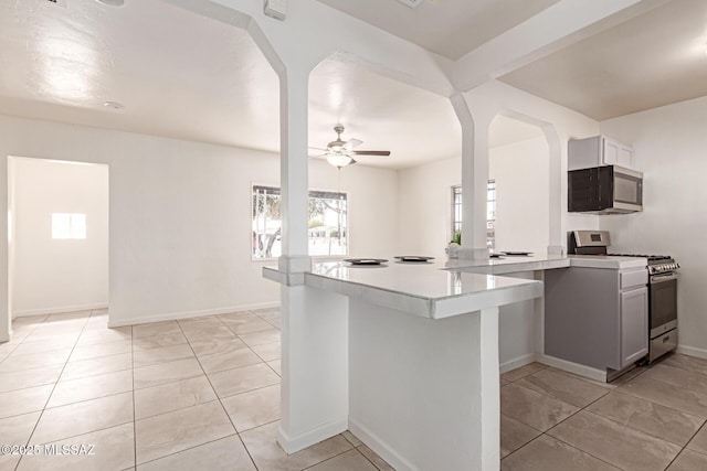 kitchen with a breakfast bar area, light tile patterned floors, appliances with stainless steel finishes, kitchen peninsula, and ceiling fan