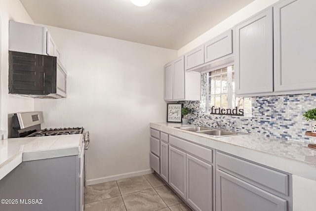 kitchen featuring light tile patterned flooring, stainless steel range with gas cooktop, sink, and tasteful backsplash