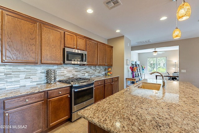 kitchen featuring light stone countertops, stainless steel appliances, sink, backsplash, and hanging light fixtures