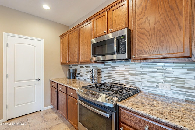 kitchen with stainless steel appliances, light tile patterned floors, light stone countertops, and decorative backsplash