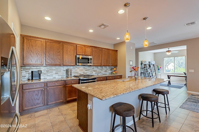 kitchen with stainless steel appliances, sink, hanging light fixtures, backsplash, and a center island with sink