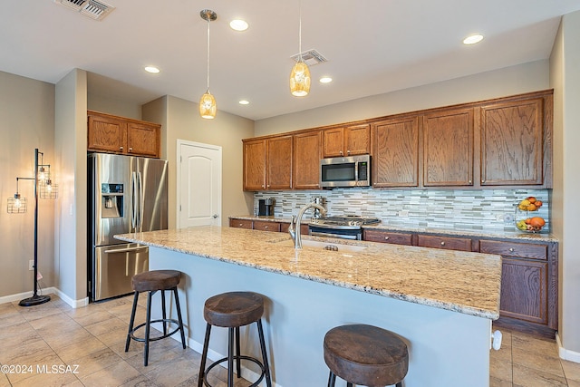 kitchen featuring pendant lighting, stainless steel appliances, tasteful backsplash, sink, and a kitchen island with sink