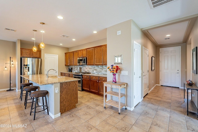 kitchen featuring light stone countertops, appliances with stainless steel finishes, a kitchen island with sink, decorative backsplash, and sink