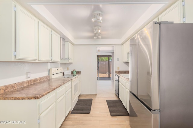 kitchen featuring stainless steel appliances, white cabinetry, a raised ceiling, and wall chimney exhaust hood