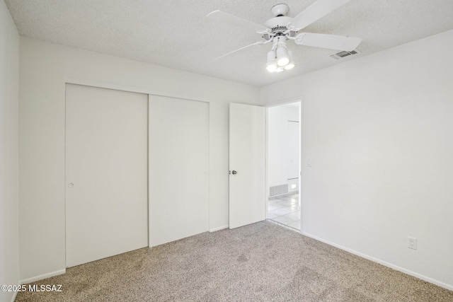 unfurnished bedroom with ceiling fan, light colored carpet, a closet, and a textured ceiling