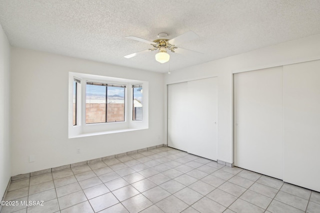 unfurnished bedroom with ceiling fan, a textured ceiling, and multiple closets