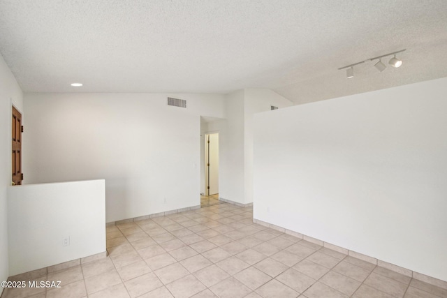 spare room with lofted ceiling, track lighting, and a textured ceiling