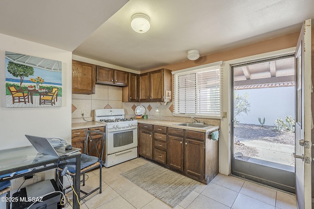 kitchen featuring white gas stove, light tile patterned flooring, a sink, light countertops, and tasteful backsplash