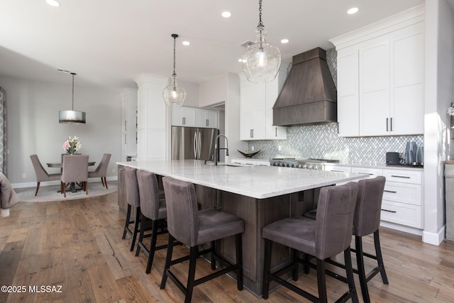 kitchen featuring stainless steel fridge, a large island, premium range hood, white cabinetry, and a sink