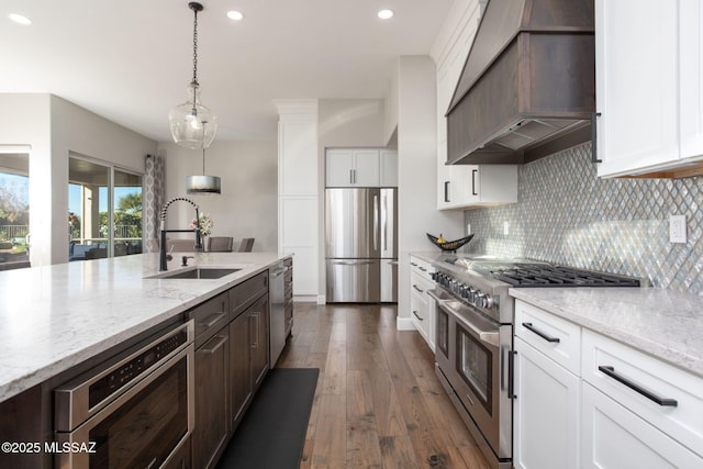 kitchen with stainless steel appliances, white cabinets, a sink, dark brown cabinetry, and premium range hood