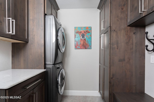 laundry room with baseboards, cabinet space, and stacked washing maching and dryer