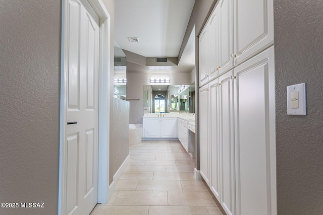 hallway with light tile patterned floors, visible vents, and a textured wall