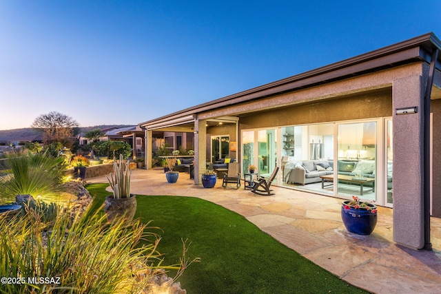 back of house at dusk featuring a lawn, a patio area, and stucco siding