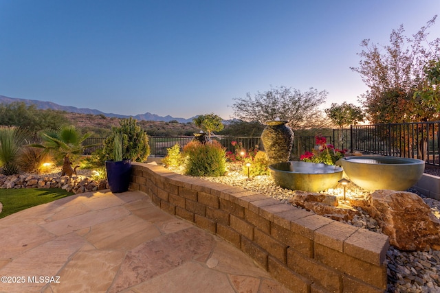 patio terrace at dusk featuring a fenced backyard and a mountain view