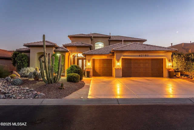 mediterranean / spanish house featuring an attached garage, driveway, a tile roof, and stucco siding