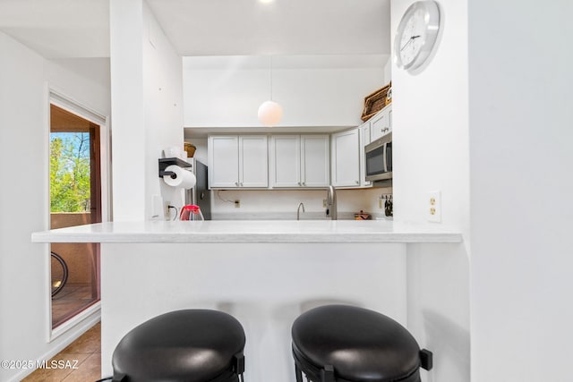 kitchen with light tile patterned flooring, white cabinetry, kitchen peninsula, and a kitchen bar