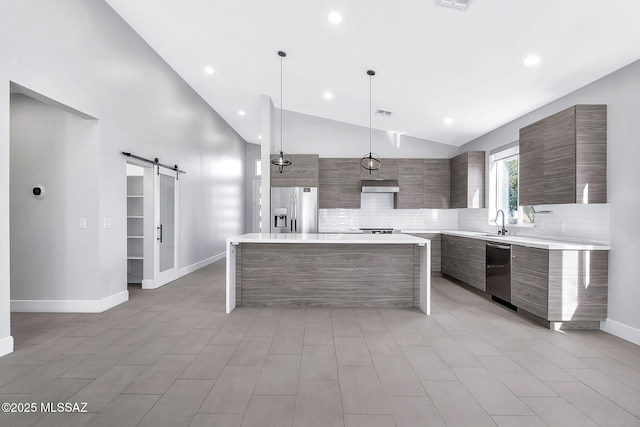 kitchen featuring a kitchen island, appliances with stainless steel finishes, backsplash, hanging light fixtures, and a barn door