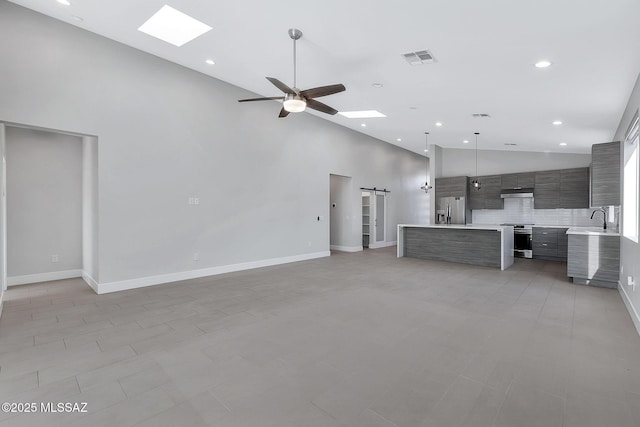 unfurnished living room with sink, a skylight, a barn door, and a high ceiling