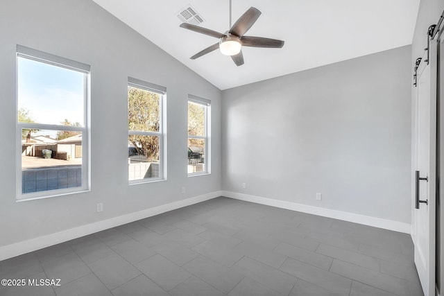 tiled spare room featuring ceiling fan, a barn door, and vaulted ceiling